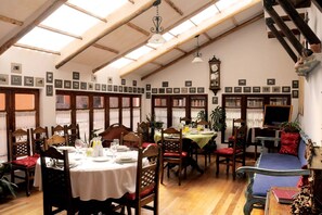 A dining area with wooden tables and chairs, a clock on the wall, and a bookshelf filled with books.