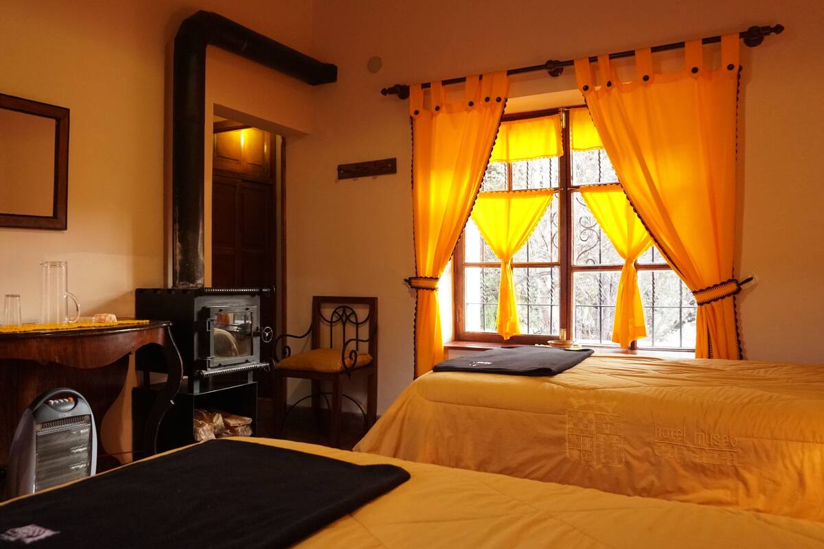 Ein Hotelzimmer mit zwei Betten, einem Schreibtisch, einem Stuhl, einem großen Spiegel und einem Fenster mit gelben Vorhängen.