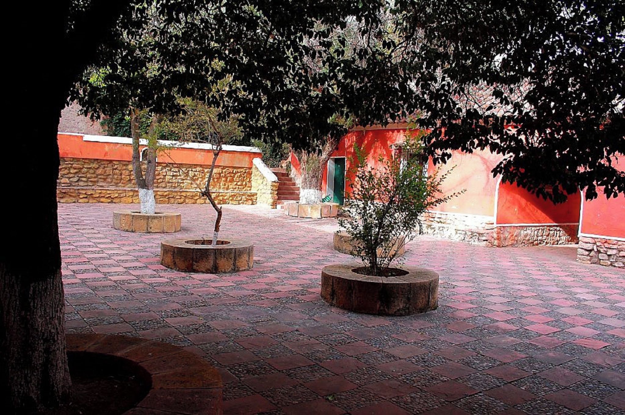 Un patio exterior con macetas de piedra, una fuente y un edificio rojo con puerta verde.