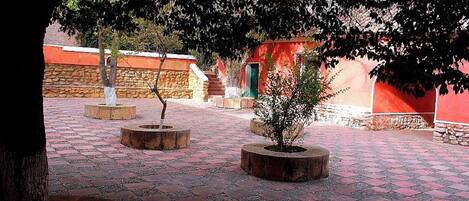 Un patio exterior con macetas de piedra, una fuente y un edificio rojo con puerta verde.