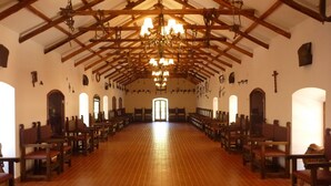 Interior de iglesia con bancos de madera, techo alto con vigas a la vista y una araña.
