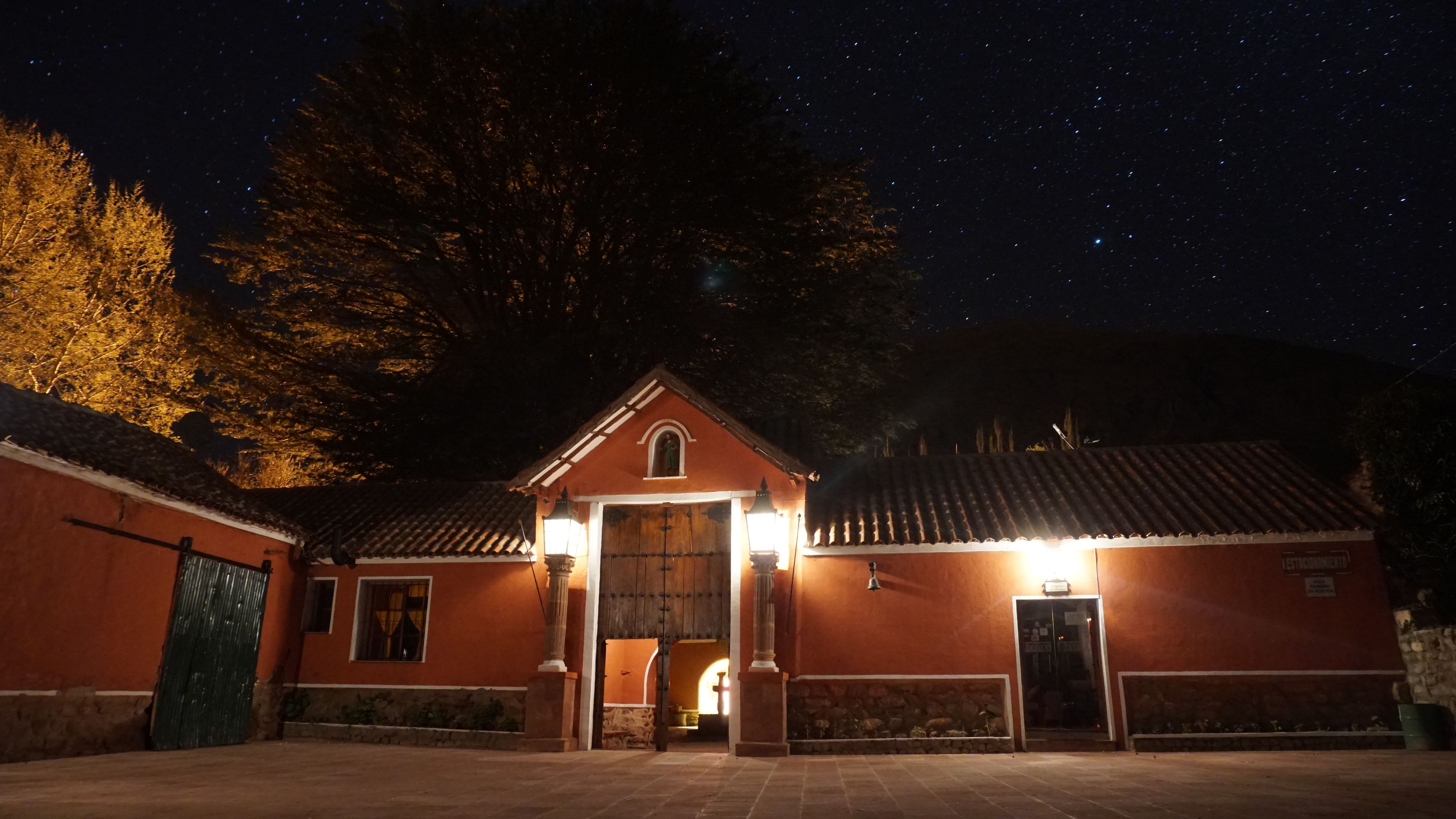 A building with a red facade, a tiled roof, and a large tree in the background.