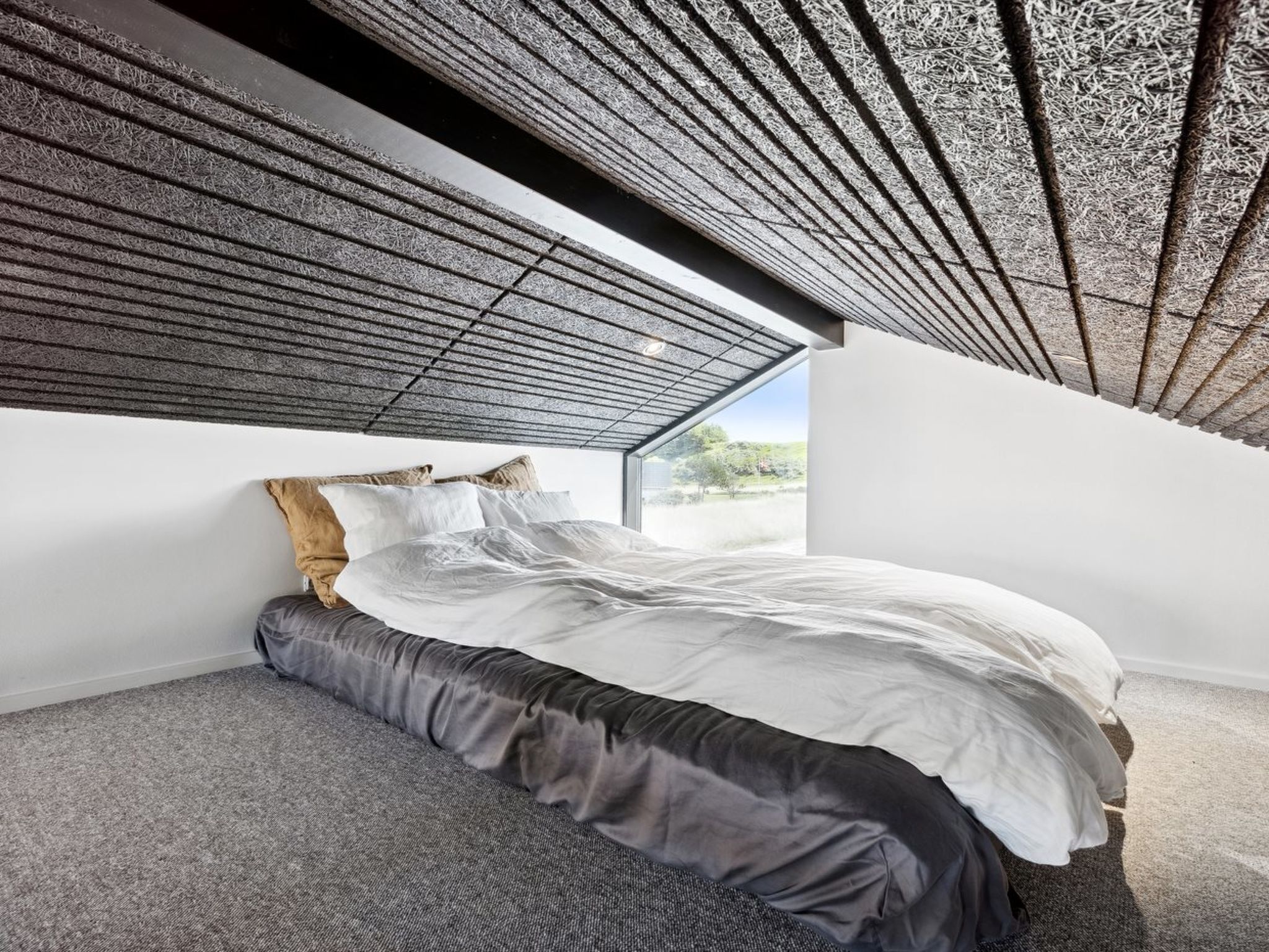 Un dormitorio moderno con techo inclinado, una cama grande y vistas al exterior.