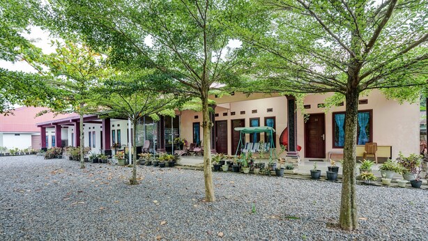 Un patio con suelo de grava, árboles y una hilera de edificios con puertas y ventanas.