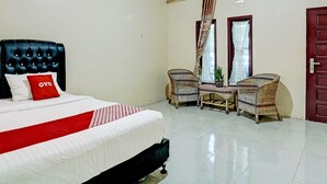 Habitación de hotel con una cama grande, dos sillas de mimbre, una mesita y un ventanal con cortinas.