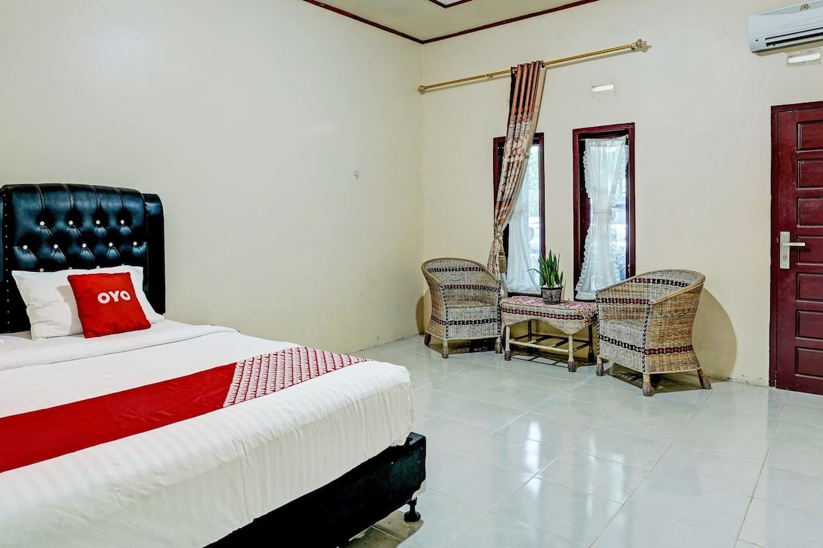 A hotel room with a large bed, two wicker chairs, a small table, and a window with curtains.