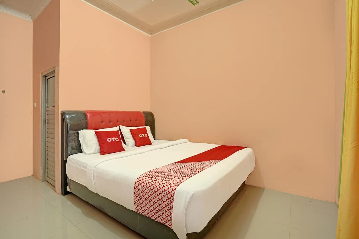 A neatly made bed with red and white bedding, a grey headboard, and a patterned throw.