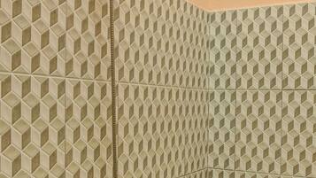Un baño con pared de azulejos de diseño geométrico, un cabezal de ducha y un inodoro.