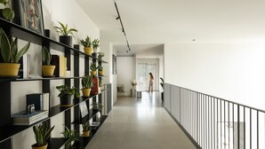 A hallway with black shelves lined with potted plants and books, leading to a door with a window.