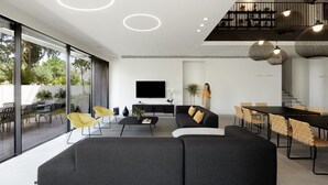 A modern living room with a sectional sofa, a dining area, and a staircase.