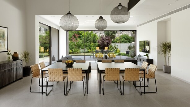 A modern dining area with a large table, multiple chairs, and hanging pendant lights.