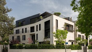 A modern multi-story building with balconies, large windows, and a stone facade.