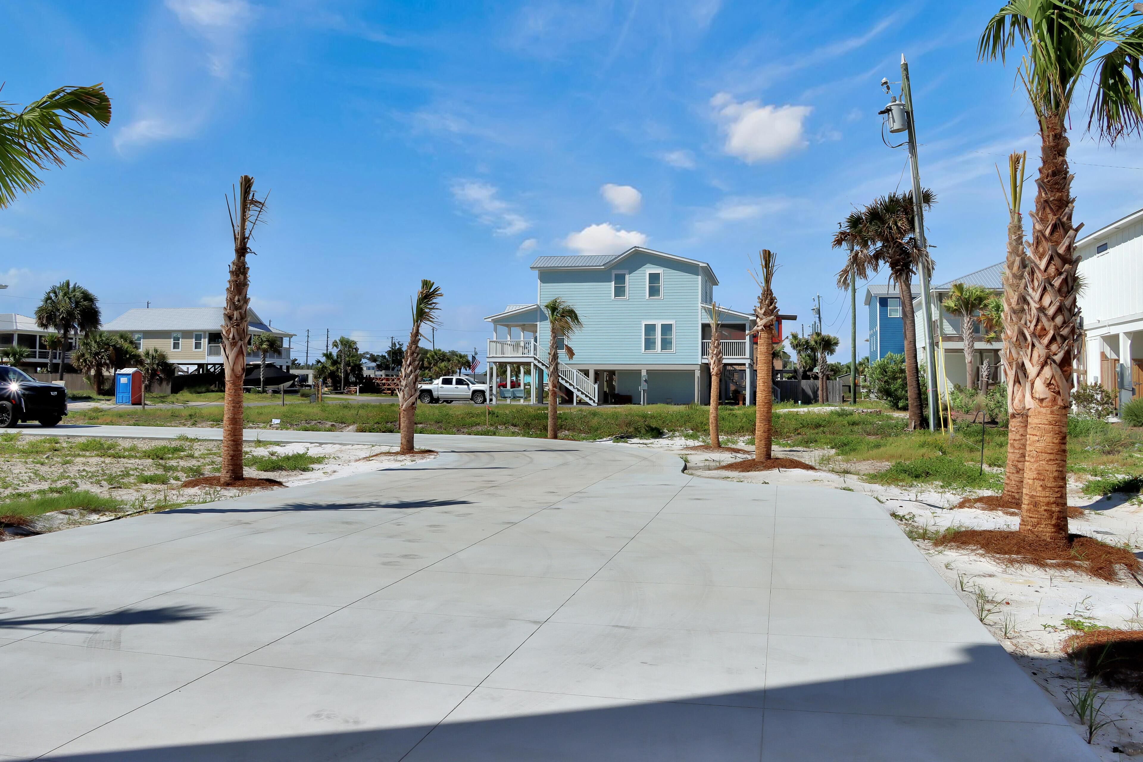 A residential area with a large light blue house, palm trees, and a concrete pathway.
