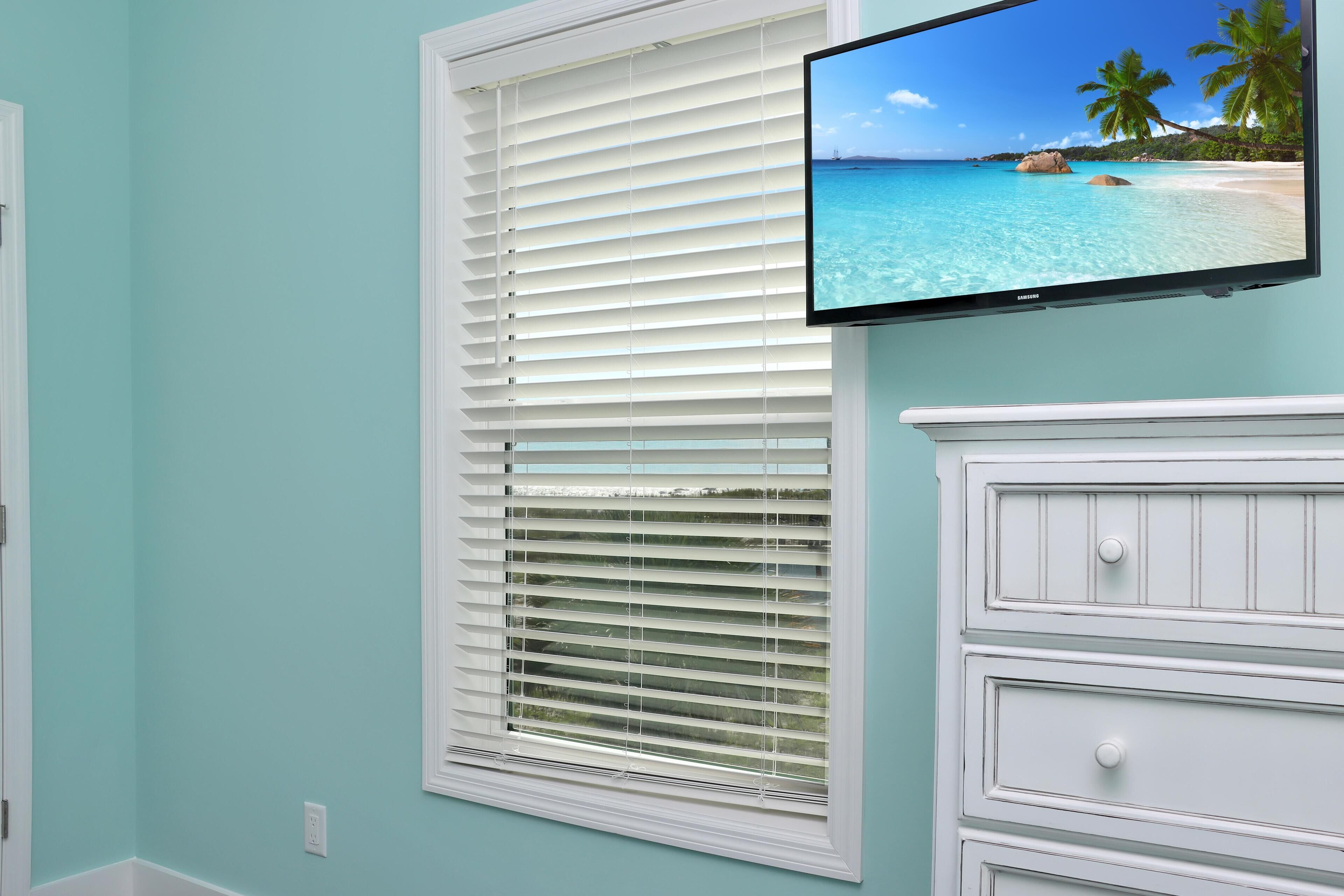 A room with a teal wall, a white dresser, and a window with blinds.