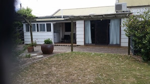 Une maison d’habitation dotée d’un patio couvert, d’une porte d’entrée et d’un petit jardin agrémenté de plantes en pot.