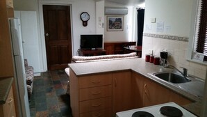 Une cuisine équipée d’une cuisinière, d’un évier, de meubles de rangement en bois, d’une télévision et d’une horloge murale.