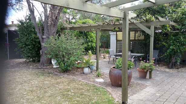 Un patio couvert agrémenté d’une pergola, de plantes en pot, d’une table et de chaises.