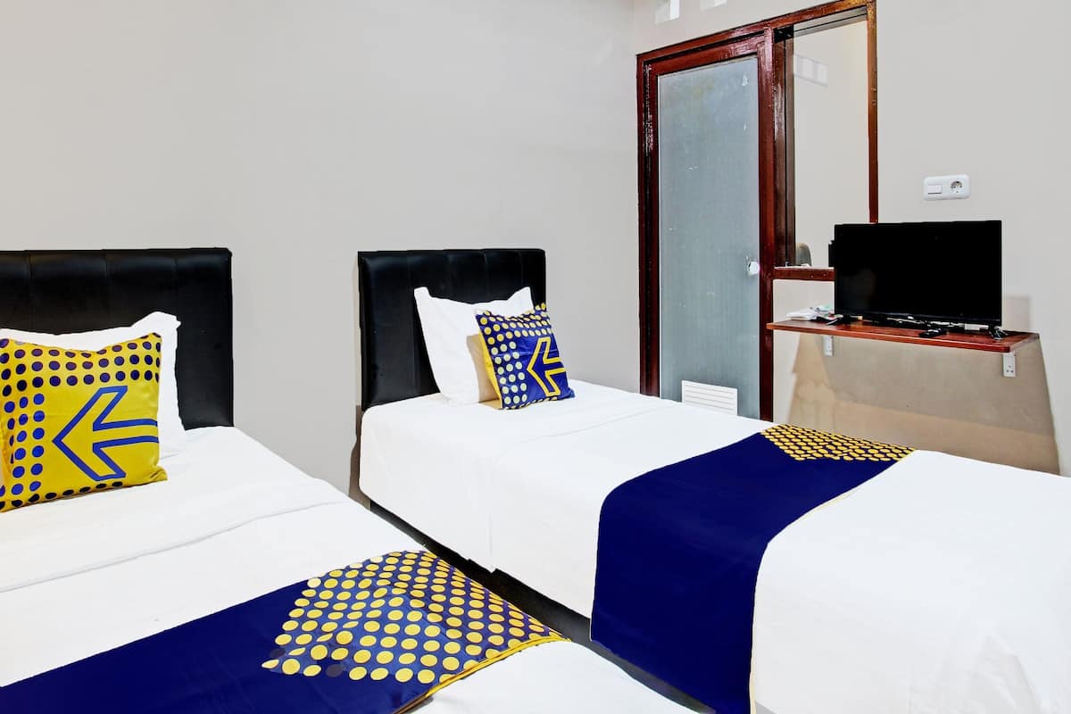 A hotel room with two beds, each with a white bedspread and blue and yellow decorative pillows. There is a television on a wooden stand to the right of the beds.