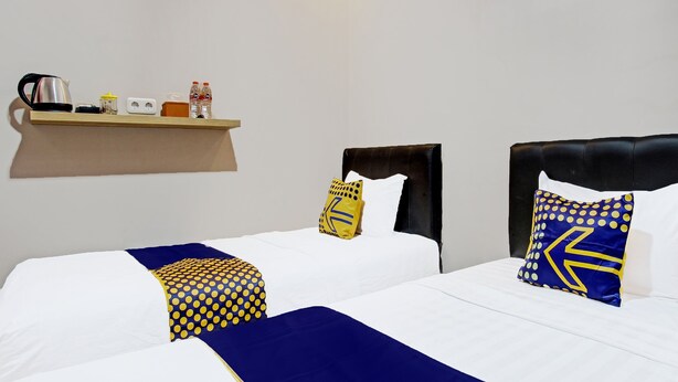 Een hotelkamer met twee bedden, elk voorzien van een blauw-geel stippenbedovertrek, een houten plank met toiletartikelen en een zwart bekleed hoofdeinde.
