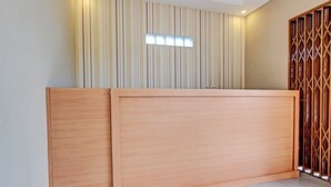 Een receptiebalie met een houten afwerking, een wand met verticale strepen erachter en een geometrisch patroon als scheiding aan de rechterkant.