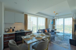 A modern living room with a dining area, a kitchen, and large windows offering a city view.