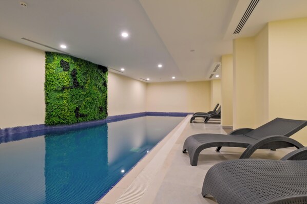 A swimming pool with a green wall and lounge chairs.