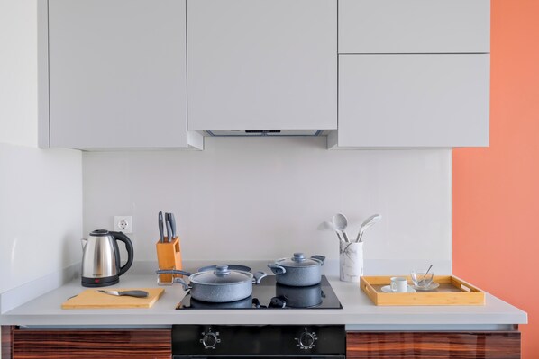 A modern kitchen with a white countertop, two electric stoves, a kettle, and a coffee maker. There are wooden utensils in a holder and a tray with a cup and a glass. - Air Basaksehir By Newinn (Istanbul)