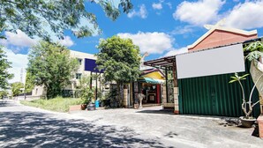 A street view with a building featuring a covered entrance, a green gate, and a tree in the foreground. - OYO 91187 Palanta Homestay Syariah (Pekanbaru)