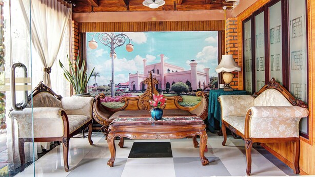 A room with a wooden ceiling, a large window with curtains, a sofa, a coffee table, and a wall painting. - OYO 91187 Palanta Homestay Syariah (Pekanbaru)