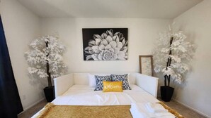Ein ordentlich bezogenes Bett mit einem Willkommen-Kissen, ein großes Blumenbild darüber und zwei Zimmerpflanzen auf jeder Seite.
