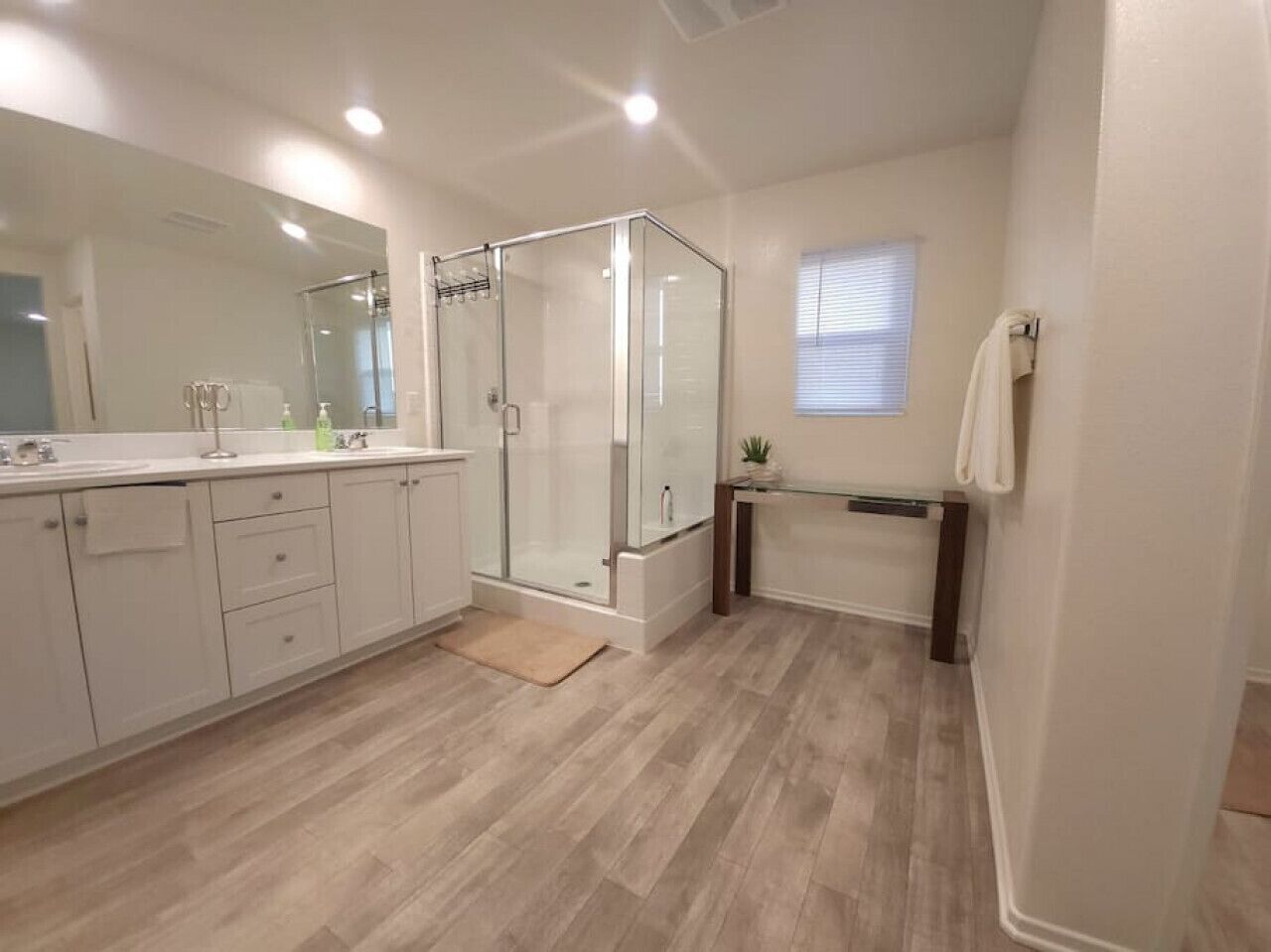 A modern bathroom with a glass shower enclosure, a vanity with a mirror, and a small window.