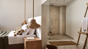 A modern bedroom with a bed, bedside table, hanging lamps, and a glass shower enclosure.