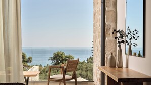 A balcony with a view of the sea, a wicker chair, a wooden table, and a vase with plants.