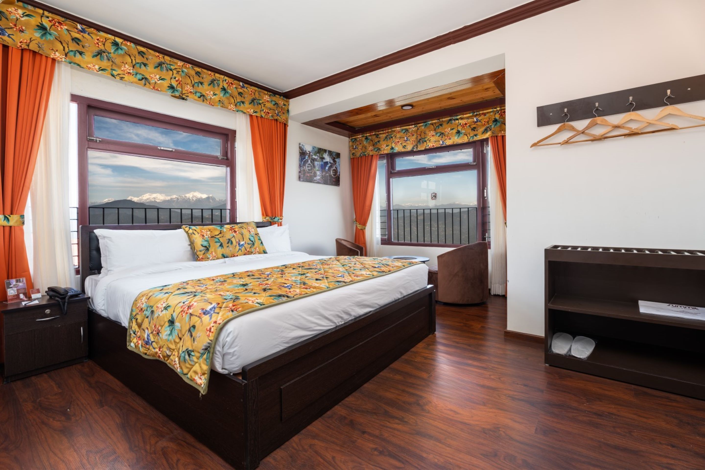 Un dormitorio con una cama grande, piso de madera, una silla, una mesita de noche, un aparador y vistas a la montaña desde la ventana.