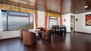 Une pièce spacieuse avec un plafond en bois, de grandes fenêtres offrant une vue sur les montagnes, un coin repas avec une table et des chaises, et un extincteur fixé au mur.