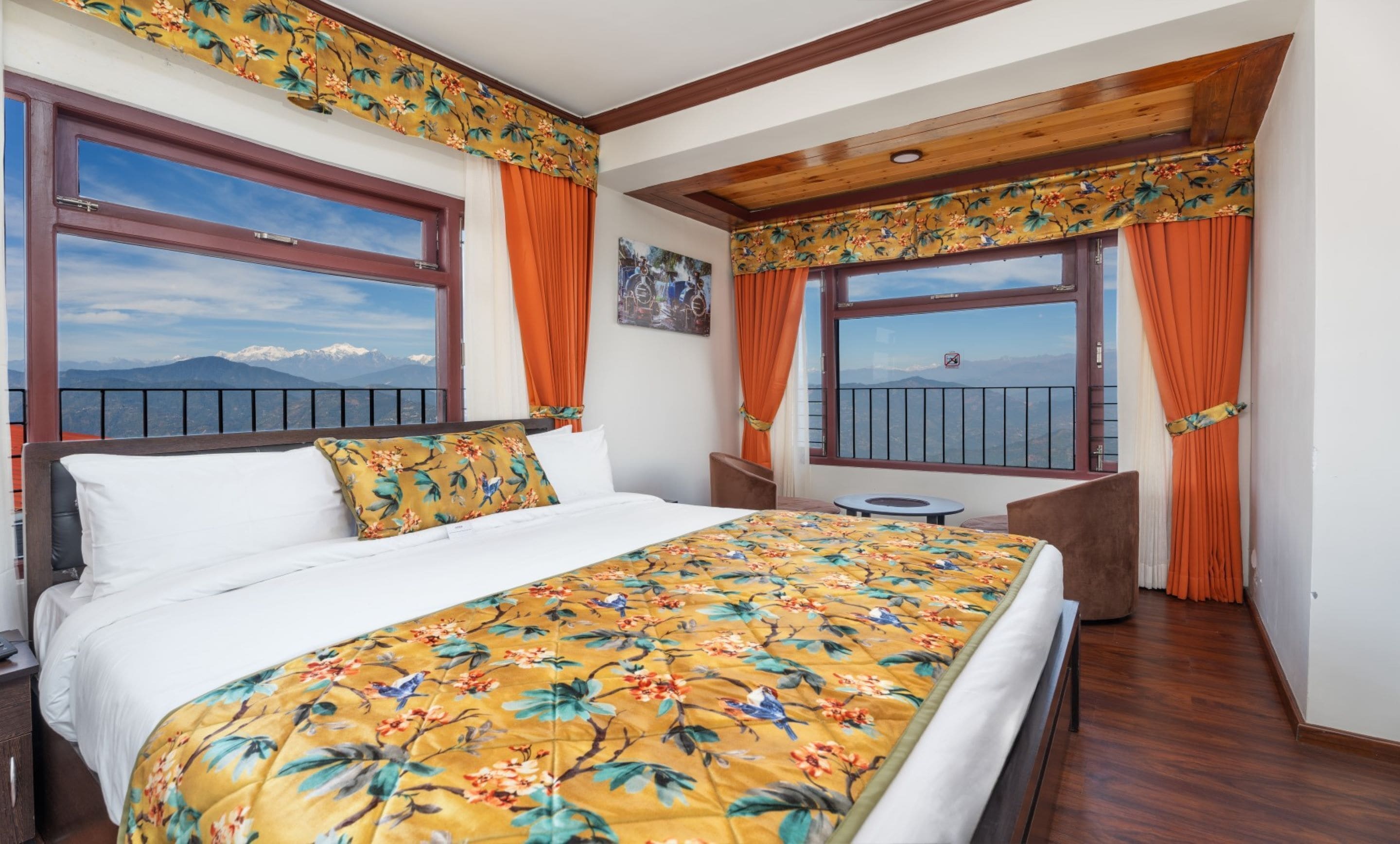 Habitación de hotel con cama, una mesita, una silla y balcón con vistas a las montañas.