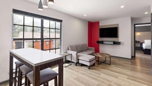 Una sala de estar moderna con comedor, un sofá, un televisor montado en la pared y un ventanal grande.