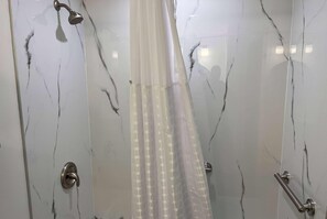 A bathroom with marble walls, a shower curtain, and a handrail.