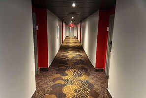 A hallway with patterned carpet, red walls, and white doors. - Ramada By Wyndham Studio Suites Dothan (Dothan)