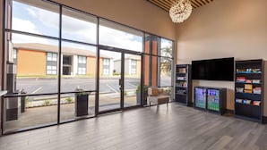A spacious lobby with large windows, a modern chandelier, a seating area, and vending machines. - Ramada By Wyndham Studio Suites Dothan (Dothan)