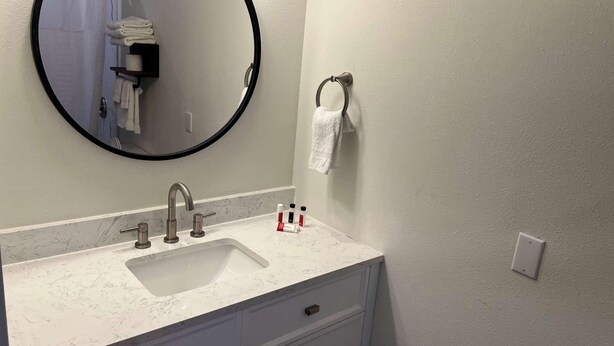 Un baño con lavamanos, espejo, toallero y dispensador de toallas.