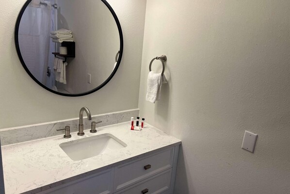 A bathroom with a sink, mirror, towel rack, and a towel dispenser.