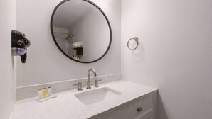 A bathroom with a white sink, a round mirror, a towel rack, and a hairdryer.
