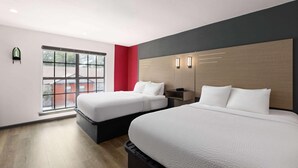 A hotel room with two beds, a window with a view, and a red accent wall.
