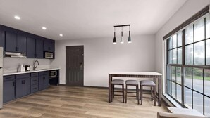 A modern kitchen with dark cabinets, a white countertop, and a dining area with a table and chairs. - Ramada By Wyndham Studio Suites Dothan (Dothan)