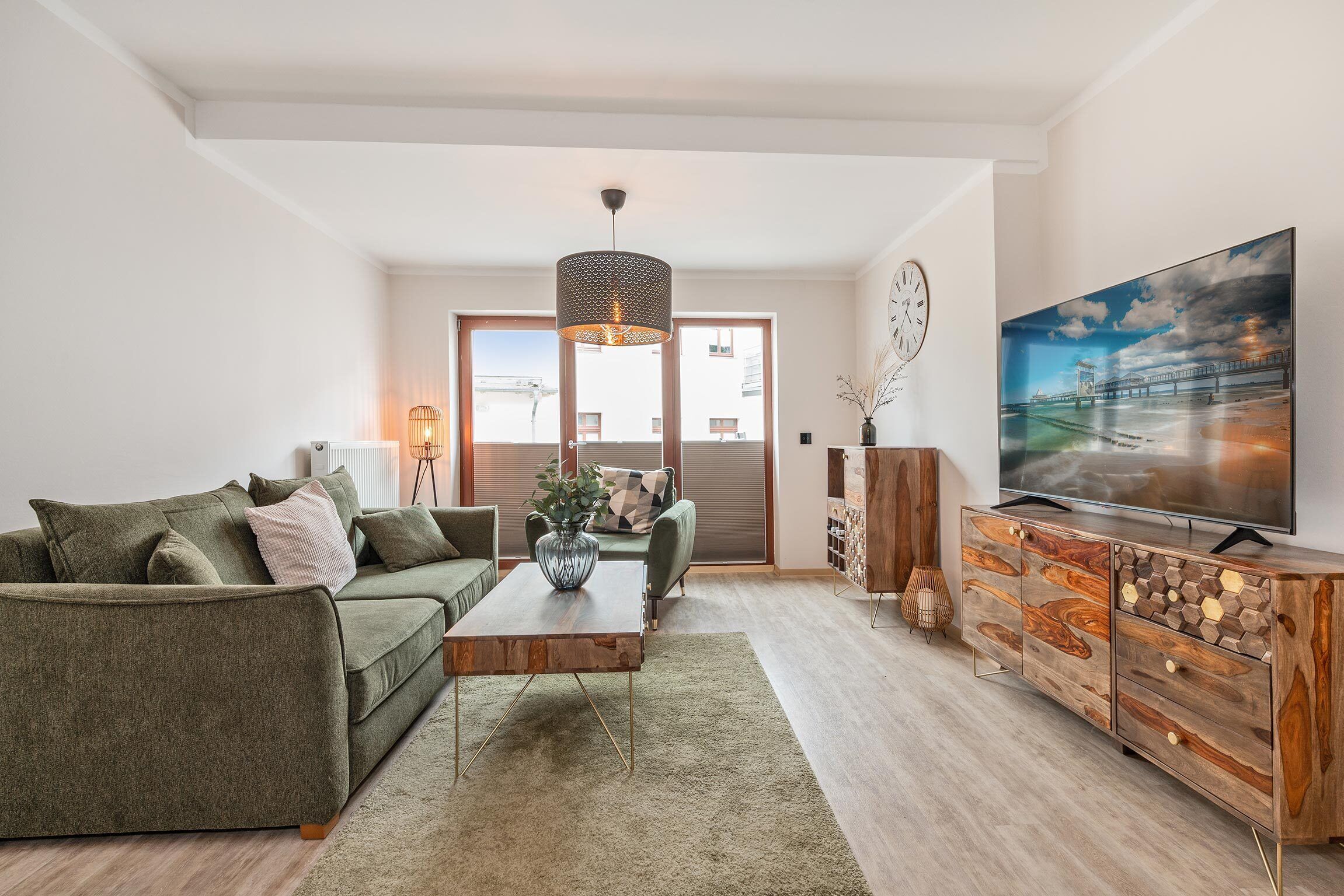 Ein modernes Wohnzimmer mit einem grünen Sofa, einem Holztisch und einem Fernseher auf einem Holzschrank.