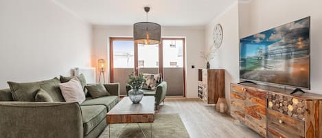 Una sala de estar moderna con un sofá verde, una mesa de centro de madera y un televisor sobre un mueble de madera.