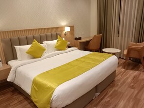 A hotel room with a large bed, a nightstand, a desk, and a chair. - Antilia By Zion (Sonepat)