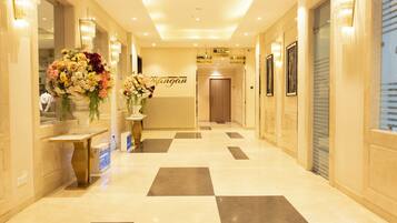 A hotel reception area with a check-in counter, a large floral arrangement, and directional signs to various hotel facilities.