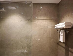 A modern bathroom with a glass shower enclosure, a towel rack with folded towels, and a wall-mounted towel rack. - Antilia By Zion (Sonepat)